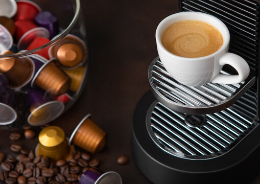 Coffee machine pods capsules with cup and raw aroma coffee beans on brown background.