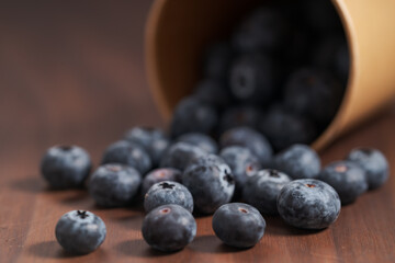 Ripe blueberries spilling from paper cup on wood table