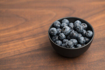 Big organic blueberries in a black bowl on walnut table