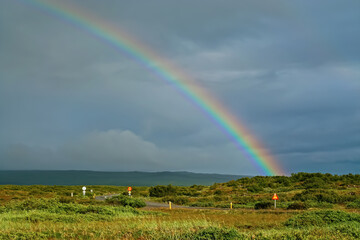 Naklejka premium Lonely road through beautiful icelandic green rural landscape after rain weather change with colorful rainbow - Iceland