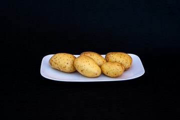 Plato blanco con patatas con piel, sobre fondo negro.