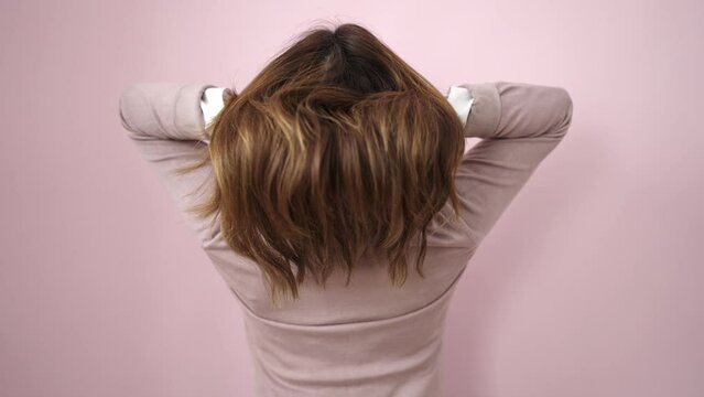 Young beautiful hispanic woman combing hair with hands over isolated pink background