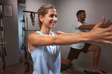 Young woman and man exercising in a gym with personal trainer on pilates machine.