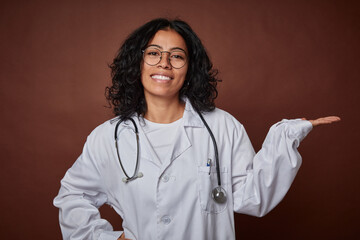 Young colombian doctor woman with stethoscope showing a copy space on a palm and holding another...