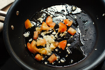 Frying garlic and tomatoes in frying pan, cooking at home
