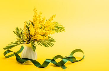 Fototapeta na wymiar Mimosa branch in a white vase and satin ribbons. Greeting card for spring holidays: Easter, Mother's Day, International Women's Day, St. Valentine's Day.