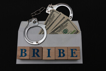 Handcuffs on an envelope with dollars on a black background and the inscription Bribe from wooden...