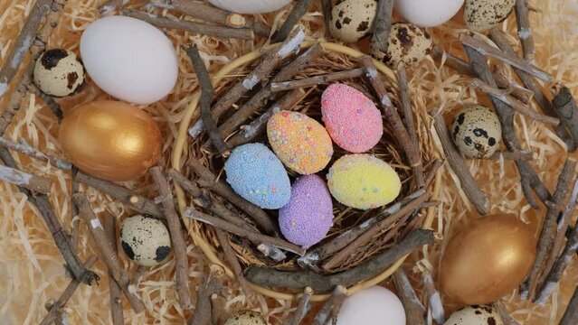 Colorful Easter eggs in the nest rotate. Greeting card with quail eggs and chicken eggs. Happy Easter holiday. Christian celebration, family traditions, flat lay top view slow motion