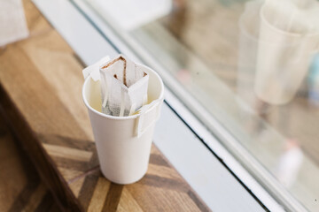 Drip bag in a paper cup on windowsill. Instant freshly brewed alternative drink in mug. Easy brew black coffee method for home, travel or office. cozy trendy lifestyle