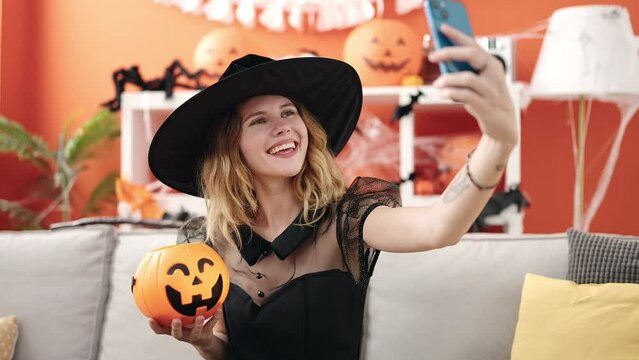 Young blonde woman holding halloween pumpkin basket make selfie by smartphone at home