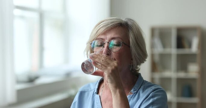 Close up happy attractive older woman hold glass, drink still water to relief thirst, to prevent body dehydration, smile enjoy natural, clean aqua. Keep daily healthy life habit, lifestyle, healthcare