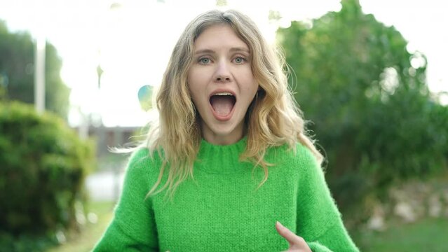 Young blonde woman standing with surprise expression at park
