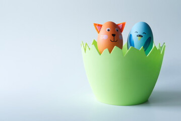 Niebieski wielkanocny kurczak i brązowy kotek zrobiony z jajka siedzący w zielonym naczyniu w kształcie skorupki jajka na jasnym tle.