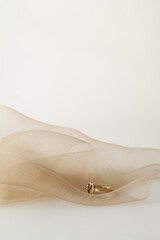Złoty pierścionek zaręczynowy na walentynki leżący na tiulu na jasnym tle