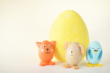 Trzy kolorowe zwierzątka zrobione z jajek stojące obok dużej wielkanocnej pisanki na jasny tle