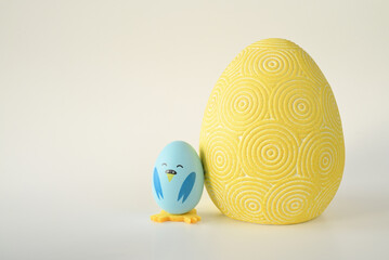 niebieski wielkanocny kurczak zrobiony z jajka stojący obok dużej żółtej pisanki na jasnym tle