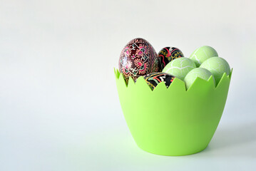 Kilka kolorowych pisanek wielkanocnych leżących w zielonym naczyniu w kształcie skorupy jajka na jasnym tle