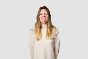 Young blonde posing for a portrait isolated, exuding natural beauty and radiance funny and friendly sticking out tongue.