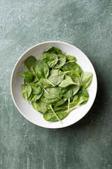 Bowl with fresh baby spinach on green vintage table, top view
