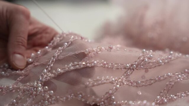 Close-up of a woman's hands sewing a wedding dress and decorating it with beads