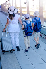 family boarding plane, woman with suitcase, two children, young traveler, boys of 8-10 years old with backpacks in outdoor terrace of airport, concept of vacation, long journey, air travel insurance