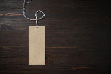 Blank kraft paper tag with cord on wood table background. Mock-up for branding identity. Flat lay.
