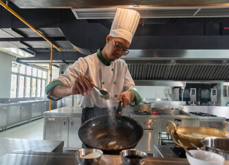 Сhef in the professional kitchen with a frying pan and a fire. Chef's hands hold iron Pan