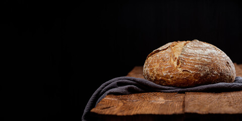 Fresh wheat rustic sourdough bread on a wooden table black background. Panoramic view, free space...