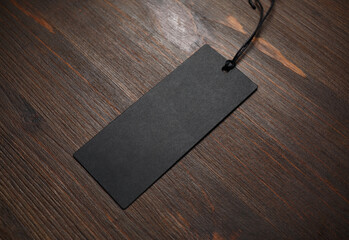 Blank black tag label with cord on wood table background. Mockup for branding identity.
