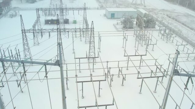Electrical grid substation and high voltage electric switchyard converter transformer in America at winter snow storm. Power station with pylons and distribution cables for EV charging stations.