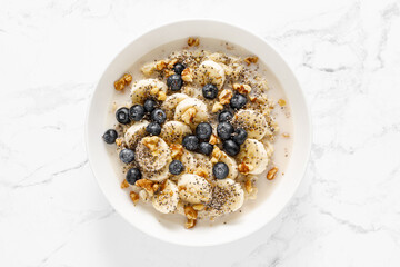 Oatmeal bowl. Oat porridge with banana, blueberry, walnut, chia seeds and oat milk for healthy breakfast. Healthy diet food. Top view - obrazy, fototapety, plakaty
