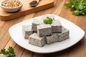 Sliced piece of Tofu mix black sesame seeds in white plate on wooden table