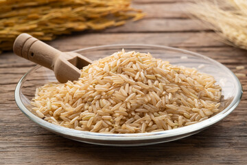 Uncooked brown rice or unpolished rice in glass plate with paddy seeds on wood table