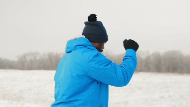 Black sportsman fighting with a shadow in the winter outdoor close up. Male boxer in a warm sportswear doing training exercises alone, takes a series of jabs and uppercuts