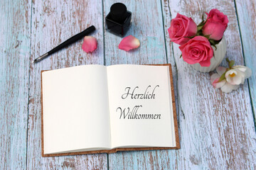 Ein Buch mit dem Text Herzlich Willkommen mit Rosen, Füller und Tinte.