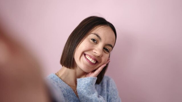 Young beautiful hispanic woman smiling confident make selfie by camera over isolated pink background