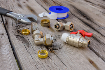 Different plumbing spare parts, sealing tape and adjustable wrench on a wooden background