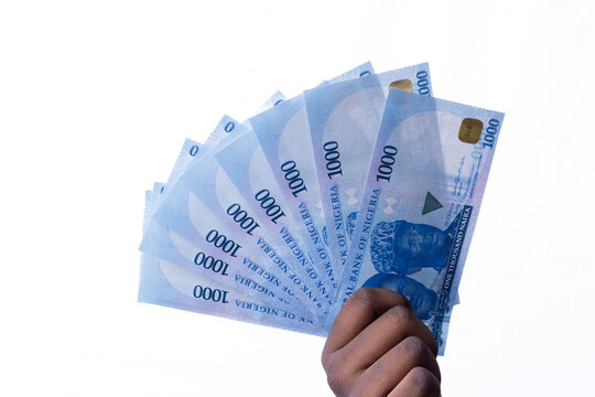 A black hand holding a spread of the New Nigerian currency / money, the 1000 Naira note on a white background