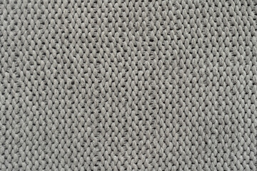 Knitted gray background. Close-up of a knitted blanket. Wavy folds material. Knitted warm grey...