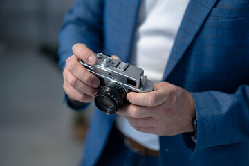 A bearded man in a suit holds a vintage film camera. Shot on a gray background.
