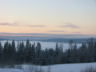 A winter sunset landscape is a breathtaking sight as the warm hues of the setting sun create a contrast against the cold, frosty mist that settles over the ground.