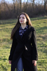 Woman looks to the side.Serious emotions.Beautiful long hair.Woman in a coat in nature.Vintage photo.Beautiful female portrait.Girl in a black coat.The wind blows hair.Sunlight falls on the grass.