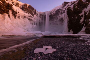 Great perspective of Skogafoss with ice floes in the foreground and beautiful red sky.