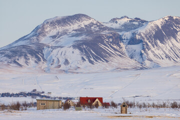 A red house in the snow in front of the Icelandic mountains at dawn.