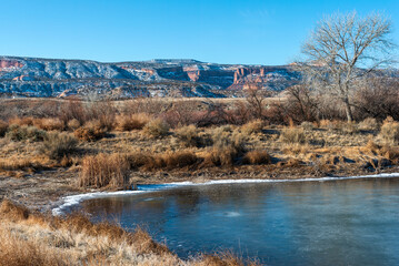 Partially frozen lake in the foreground with snowy cliffs of the McInnis Canyons CSA in the background.