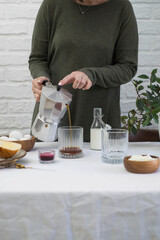 a woman is pouring coffee in glass on light table for breakfast.