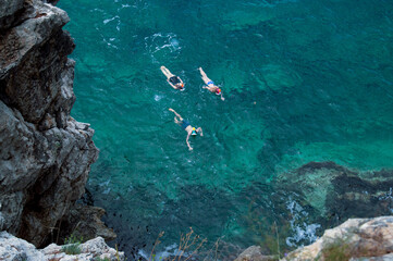 Three children in snorkeling masks swim in clear sea water towards the shore. Aerial top view of...