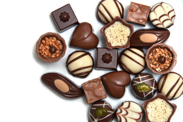 Close up of a selection of luxury chocolates, with a variety of shapes including a heart, florentines, and pistachios. They are in white, milk and dark chocolate and against a white background.