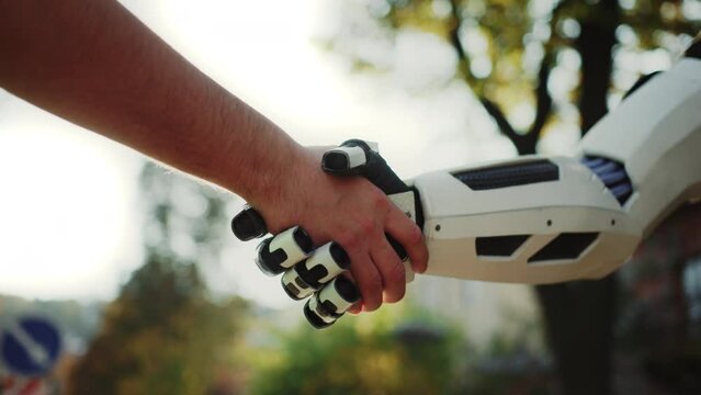 Close-up shot of unrecognizable Caucasian man shaking robot hand on sunny day outdoors. Human and artificial intelligence concept. Blurred view of autumn park on background