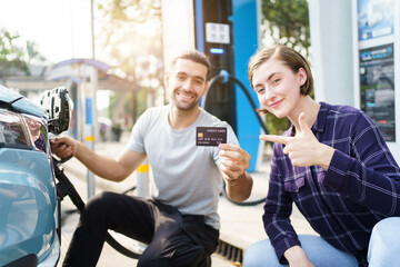 Lovely young caucasian couple charging their electric vehicle or EV car at fast charging EV station. Cashless or online payment for electric vehicle charging station. Sustainable energy concept.